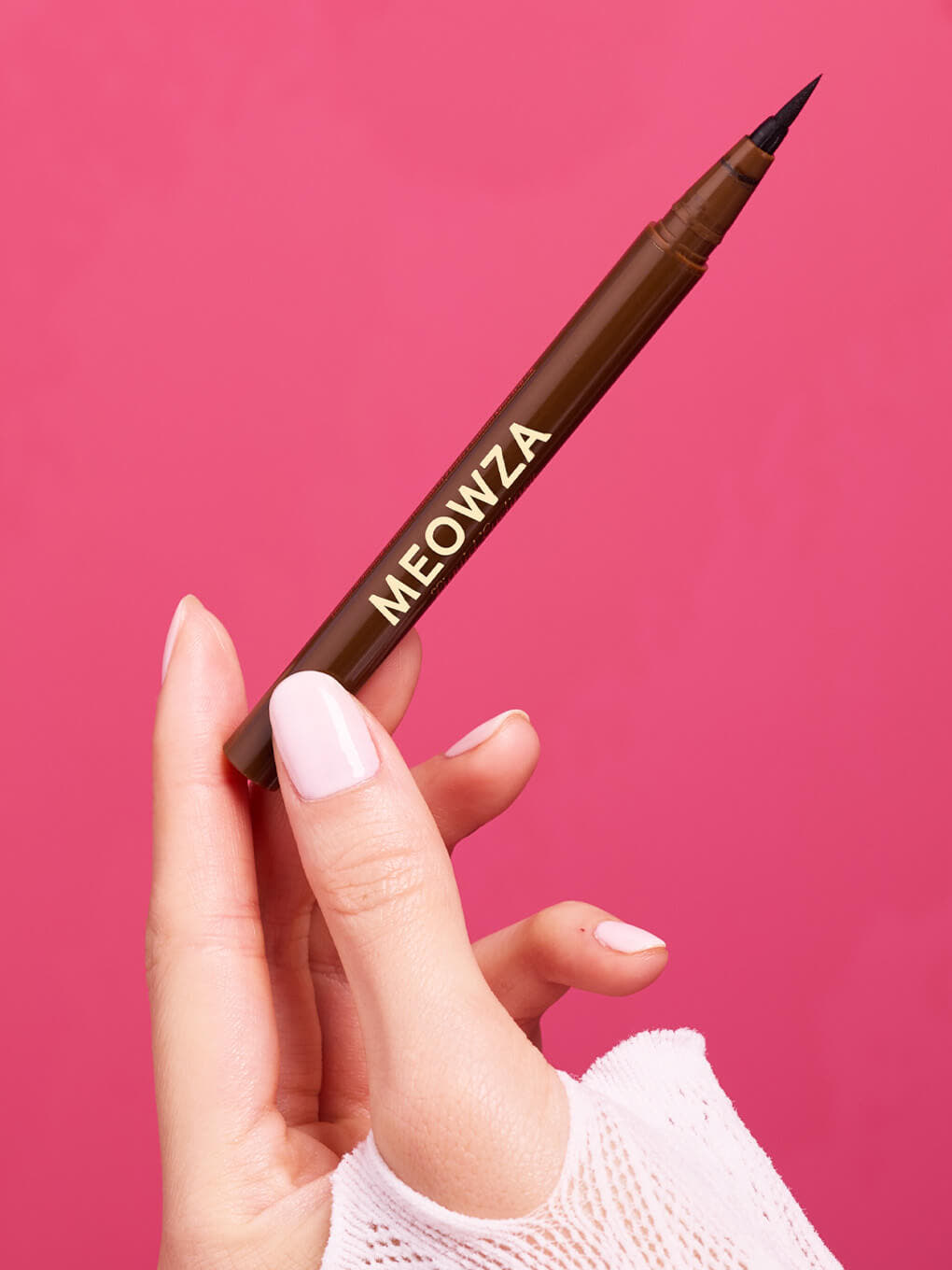 Chocolate -- hand holding brown liquid mascara on pink background